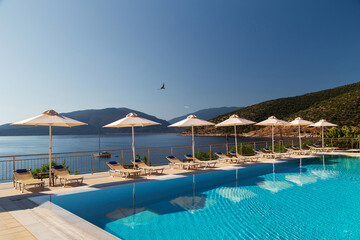 Luxury swimming pool with empty deck chairs and umbrellas at resort with beautiful sea view. Greek...