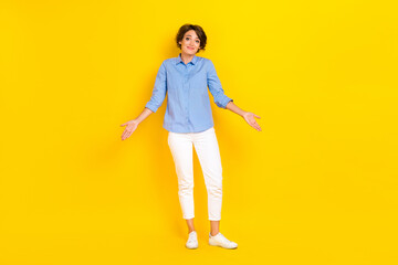 Full length photo of pretty unsure lady wear blue shirt shrugging arms shoulders isolated yellow color background