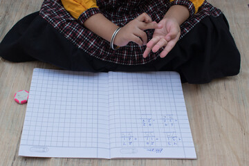 Girl Kid or toddler solving maths problem in notebook. Counting with finger and writing. Girl...