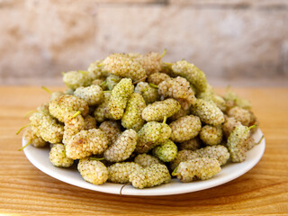 Fresh white mulberry on plate on wooden background. (Morus alba) Side view close-up. Summer organic fruits. Mulberry background