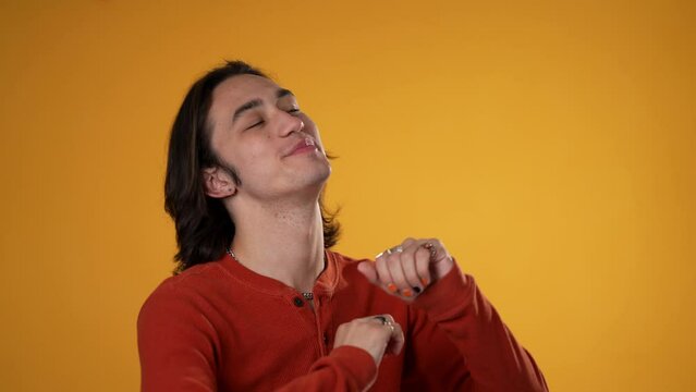 Slow motion portrait of happy smiling dancing Hispanic Latino gender fluid non-binary man wearing orange shirt isolated on yellow background.