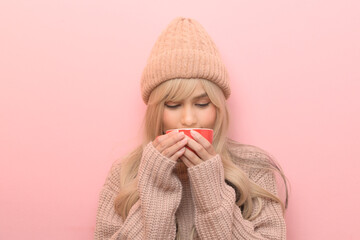 Portrait of Caucasian young woman wearing sweater drinking coffee over pink background