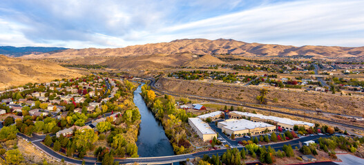 Aerial panoramic view of a beautiful Truckee River in Autumn with colorful trees, barren desert mountains, and a partly cloudy blue sky west of Reno Nevada.
