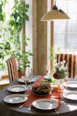 The table is set for a family dinner. Plates and glasses on a red tablecloth, meat and chicken with vegetables. Bouquet of flowers on the table