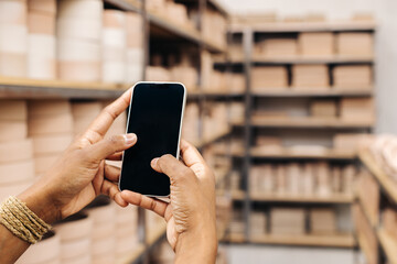Unrecognizable ceramist using a smartphone in her shop