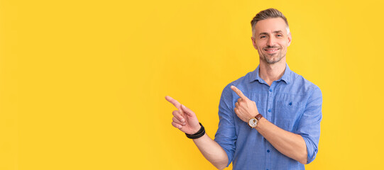smiling adult man with wrist watch point finger on yellow background, copy space, meeting minutes....