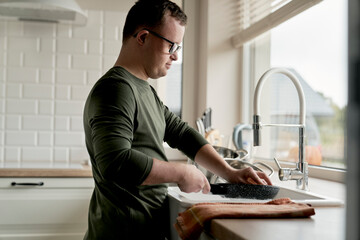 Adult caucasian man with down syndrome washing dishes at home
