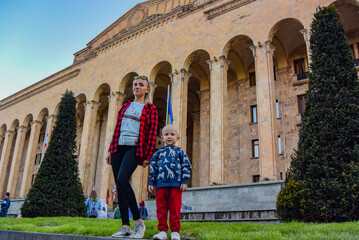 A girl with a child on the background of the Parliament building on Rustaveli Boulevard on April 27, 2019 in Tbilisi, Georgia.