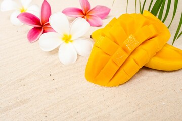 Mango with green palm leaf and plumeria flowers on a sand background