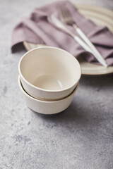 Two small empty salad bowls, plates and linen napkins on gray background
