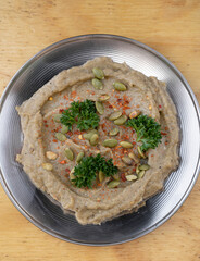 Middle Eastern cuisine. Closeup view of traditional baba ganoush spread, made with pureed aubergines and sesame seeds, in a metal dish on the wooden table.