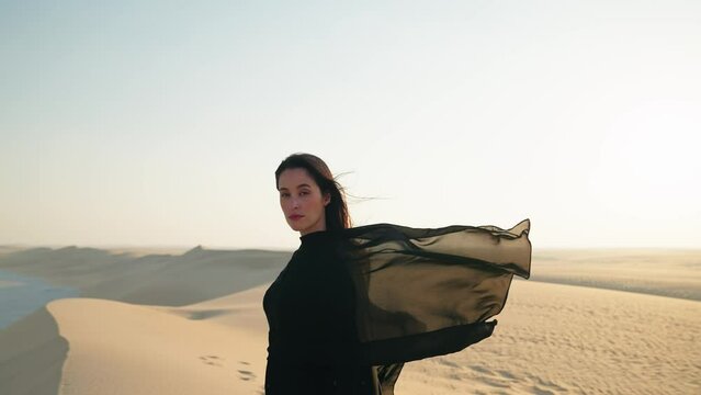 Young beautiful girl in traditional Abaya dress stand along the dunes in the desert of Qatar
