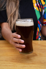 Drinks. Closeup view of a young caucasian female hand holding a glass of black beer in the bar.