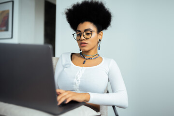 focused african american woman in eyeglasses using laptop at home.