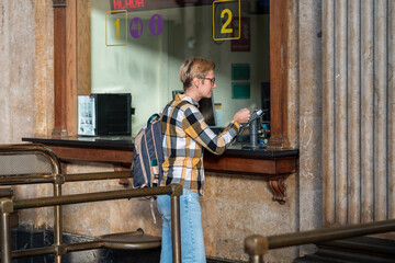 Adult 35s year old lesbian woman in plain shirt and jeans with backpack and sunglasses traveling by train in Europe. Pay with bank card for the ticket on train station in Barcelona, Spain.
