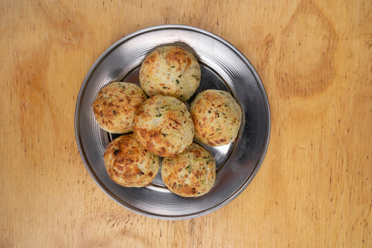 South American food. Closeup view of small, baked, cheese-flavored rolls, called chipa, in a metal dish with a wooden background.