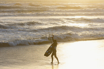 Beautiful girl does the extreme sport of kite surfing with rough sea, high waves and strong wind at sunset