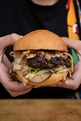 Monster burger. Woman holding a multilayer hamburger with mozzarella cheese, meat, cucumber...