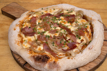 Closeup view of a pizza with tomato sauce, mozzarella cheese, crispy bacon and onions, on the wooden table.