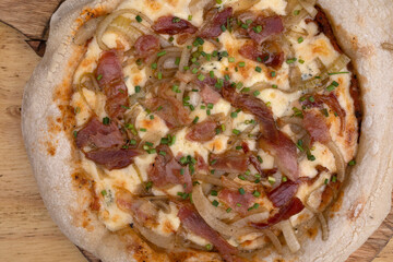 Closeup view of a pizza made with tomato sauce, mozzarella cheese, crispy bacon and onions, with a wooden background.