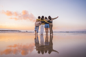 Back view of the four girls embracing and enjoying of the golden sunset at the ocean - 542993263
