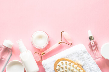 Natural cosmetics on pink. Skin care product, cream, soap serum, jade roller and white towel. Flat...