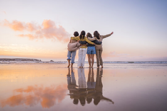 Back view of the four girls embracing and enjoying of the golden sunset at the ocean