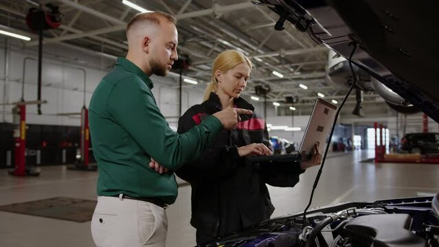 Car repair service center. A female mechanic holds a diagnostic laptop and shows the test results to the manager