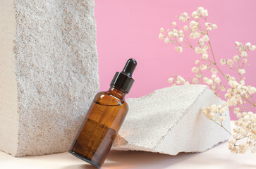 Essential oil or serum on a background of natural stones and gypsophila. Brown bottle with pipette