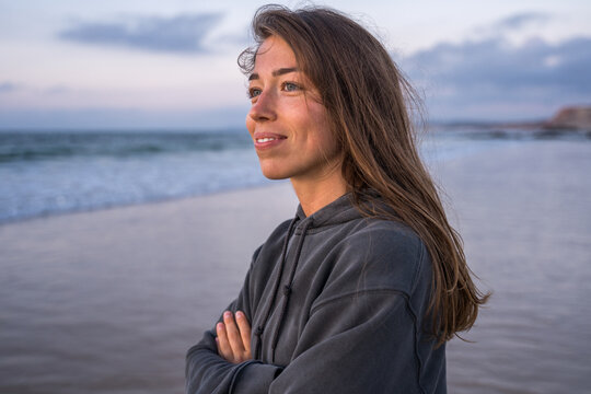 Smiling brunette girl looking at the distance while standing arms crossed at the ocean beach
