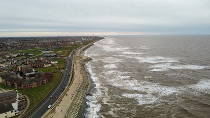 Aerial view of waves crashing onto the beach with views of Blackpool in the distance. 