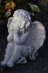 Petite statue d'un ange aux cheveux bouclés qui est assis l'air pensif, les coudes posés sur les genoux et la tête un peu relevée dans la paume de ses mains