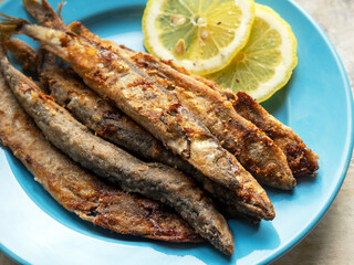 Fried capelin on a blue plate with lemon in close-up. Homemade food.