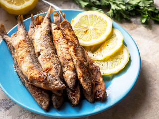 Fried capelin on a blue plate with lemon in close-up. Homemade food.