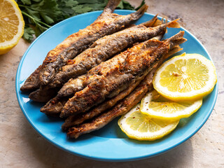 Fried capelin on a blue plate with lemon in close-up. Homemade food.