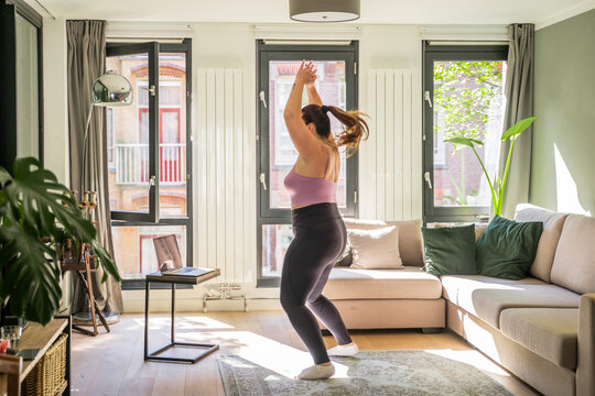 Sportive full figured woman exercising at home, doing jumping jacks