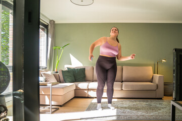 Fototapeta na wymiar Full length view of the overweight woman dancing alone at her cozy apartments