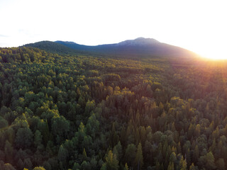 Aerial view of mountain range and forest with sun setting behind the mountain