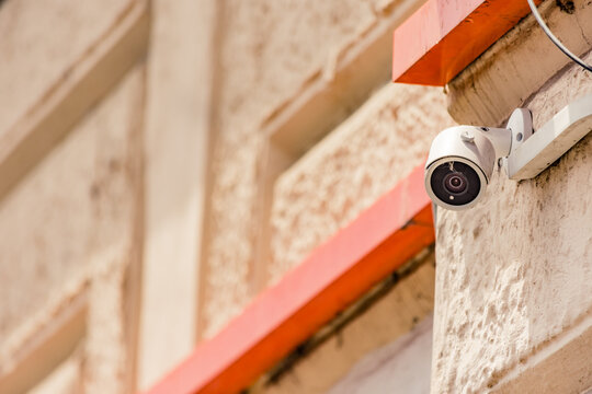 Small security camera with cracked lens installed on a building exterior wall