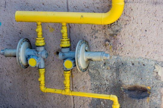 Yellow gas pipes with two pressure regulators next to a concrete wall