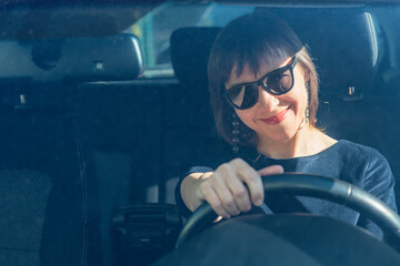 Woman sits in a car in sunglasses, holds the steering wheel and smiles - 543004289