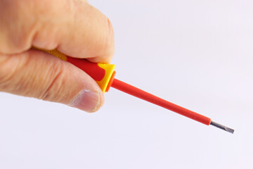 The hand holds a screwdriver with an insulated handle on a white background.Soft focus.