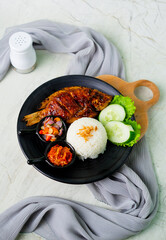 Grilled gourami or Gurame bakar with red barbeque sauce, vegetables, and chilli sauce on a white plate. Asian Food. 