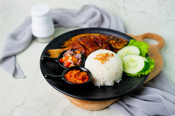 Grilled gourami or Gurame bakar with red barbeque sauce, vegetables, and chilli sauce on a white plate. Asian Food. 