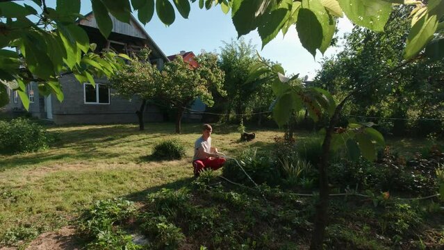 Man sits and waters the garden slow motion sunny summer day