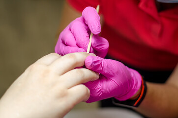 Obraz premium Female manicurist in pink gloves works with young hands and nails under a bright lamp. Process of lifting the cuticle with an apricot stick