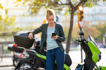 Red-haired woman using the smart phone next to her parked motorcycle