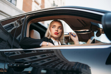 Young woman with elegant hairstyle and red lips sitting in car