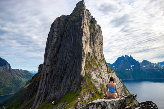 a beautiful girl sits on the rocks enjoying the view of the famous segla mountain in norway, senja island; hesten trail head, the famous norwegian fjords with mighty mountains above the sea