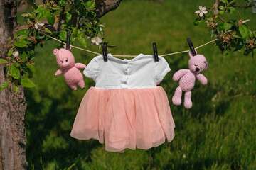A newborn baby's dress and small cotton-knitted toys hang drying on a clothesline in the garden....